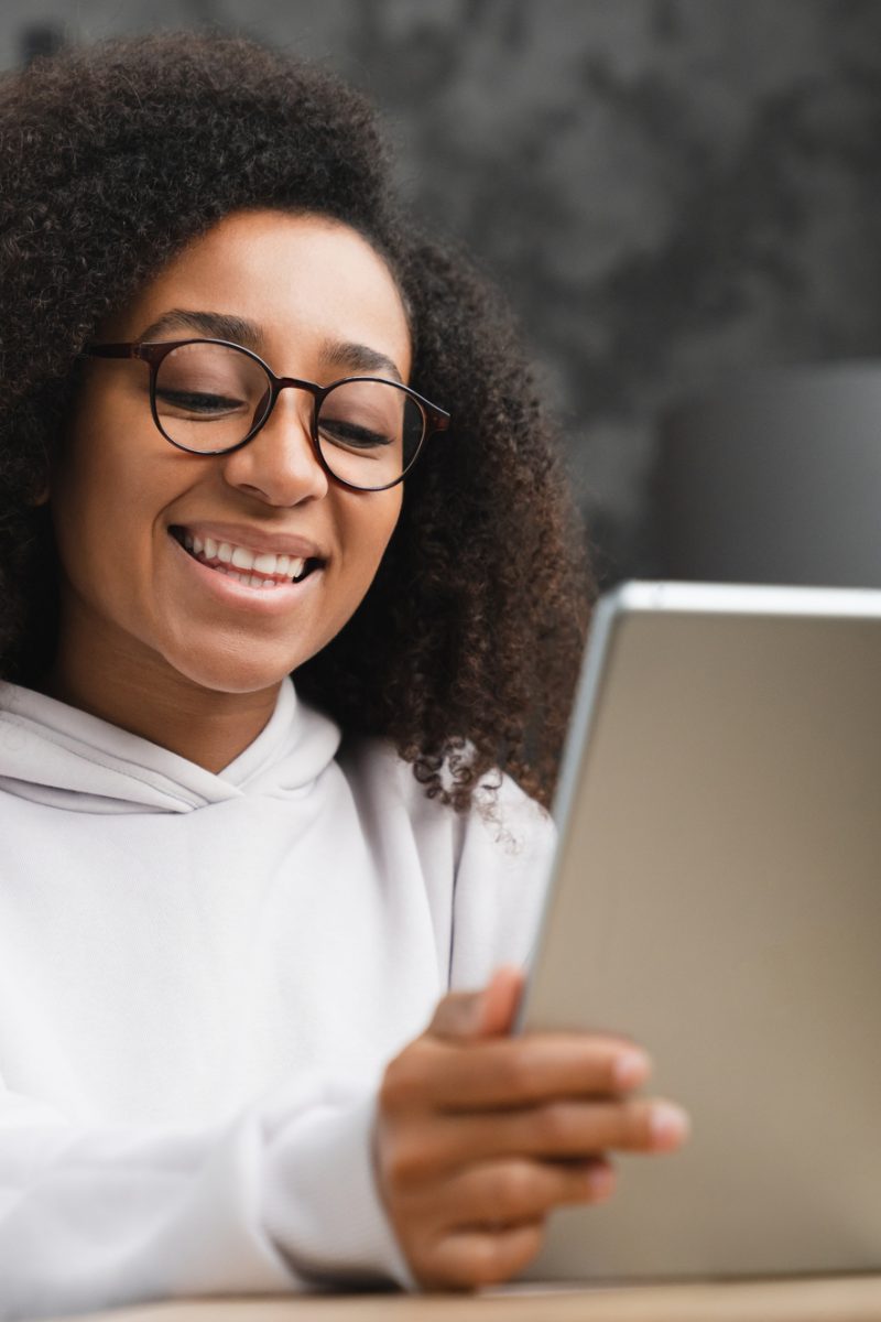 Closeup cropped shot of smiling cheerful african woman teenage girl schoolgirl using digital tablet at home, doing homework assignment online, browsing social media