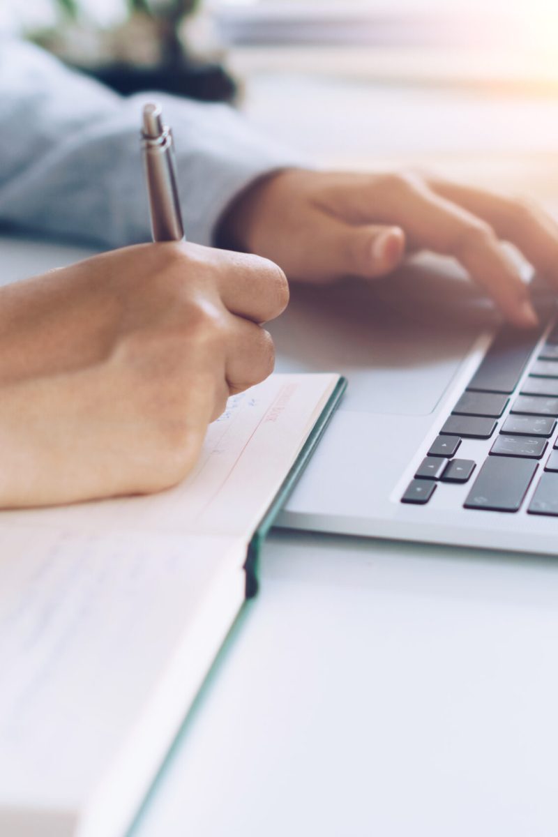 Woman is writing in planner notebook while using laptop to work or plan with workspace at home. Education business lifestyle concept.